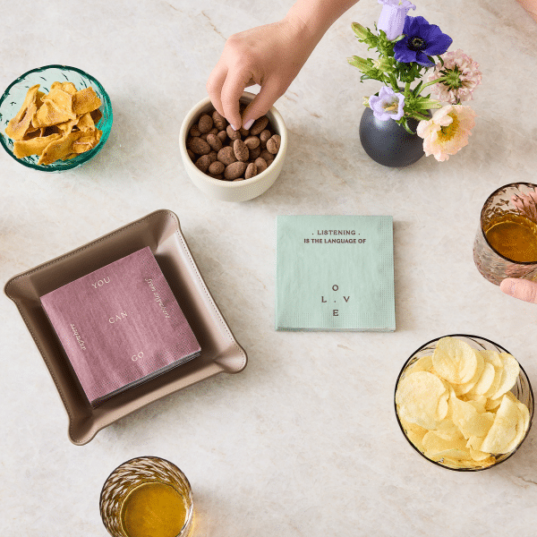 tabletop with a mint green napkin surrounded by snacks, drinks, and flowers in a minimalist setting