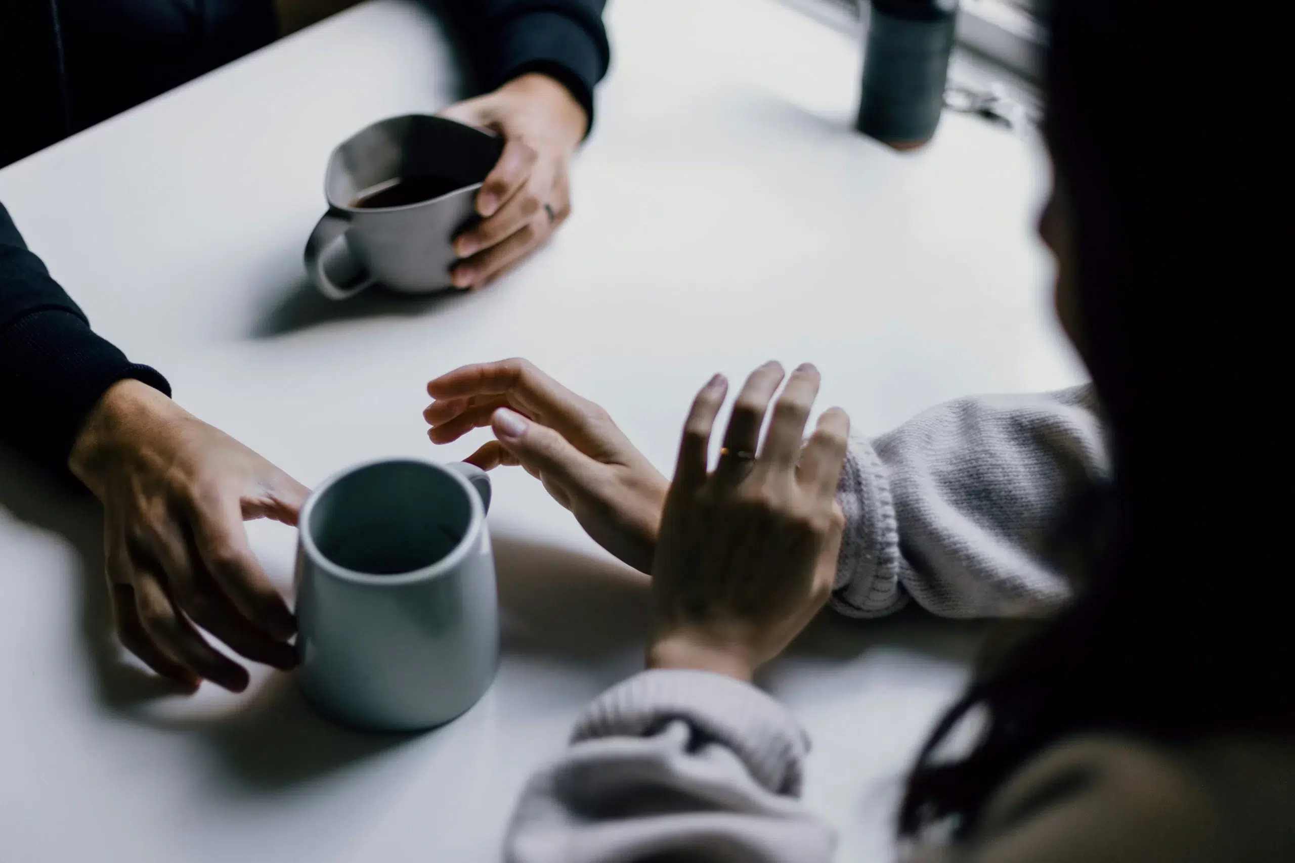 Close-up of two people sharing coffee, focusing on their hands resting on a table with coffee cups, creating a warm, conversational scene.